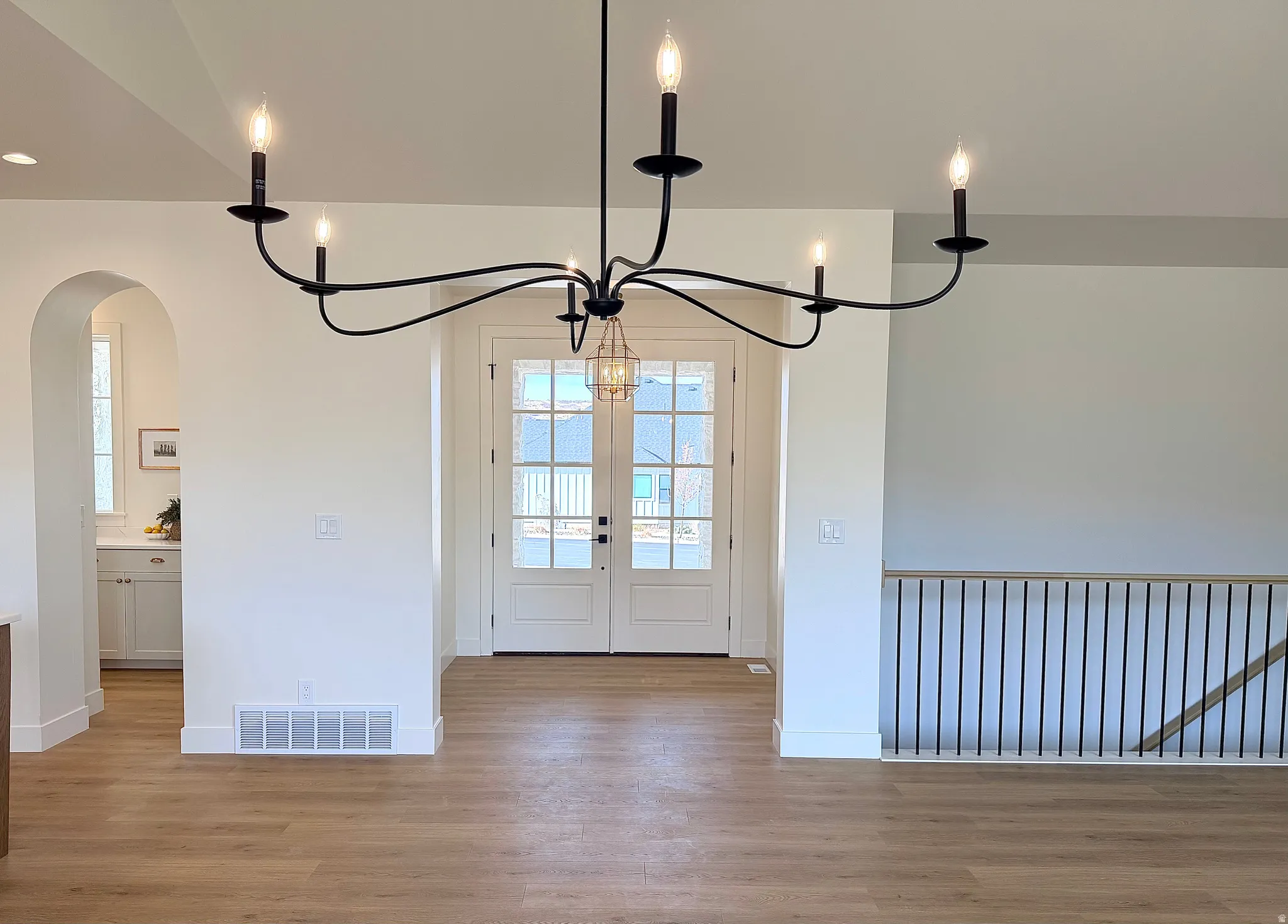 Foyer entrance with light wood-style flooring, french doors, arched walkways, and a chandelier