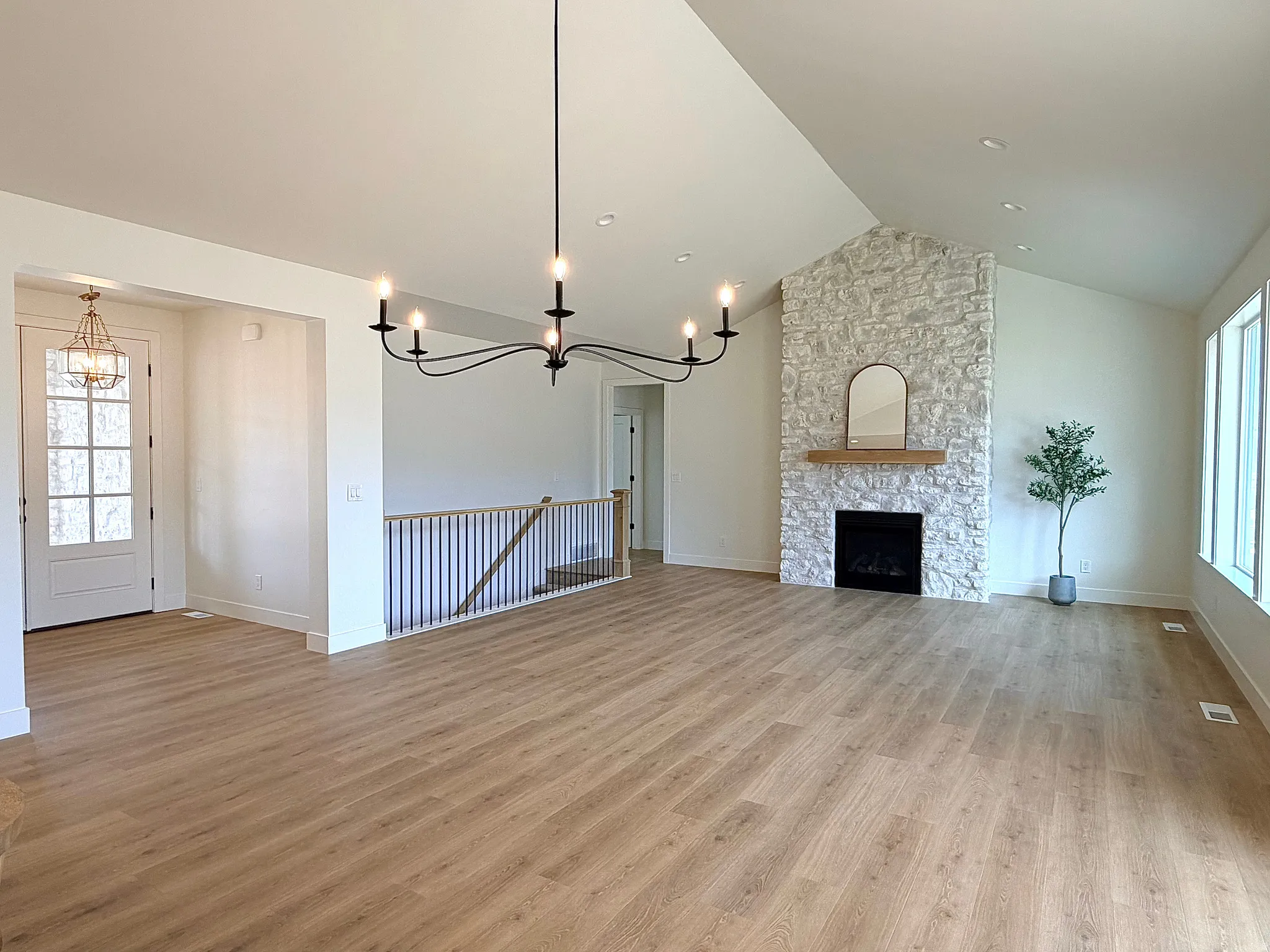 Living room featuring a chandelier, light wood-type flooring, a stone fireplace, and lofted ceiling