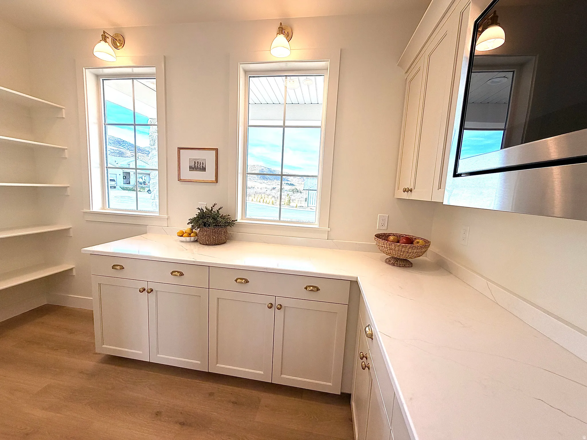 Butlers pantry featuring white oak cabinetry, plenty of storage area, stainless steel microwave, light wood finished floors, and healthy amount of natural light