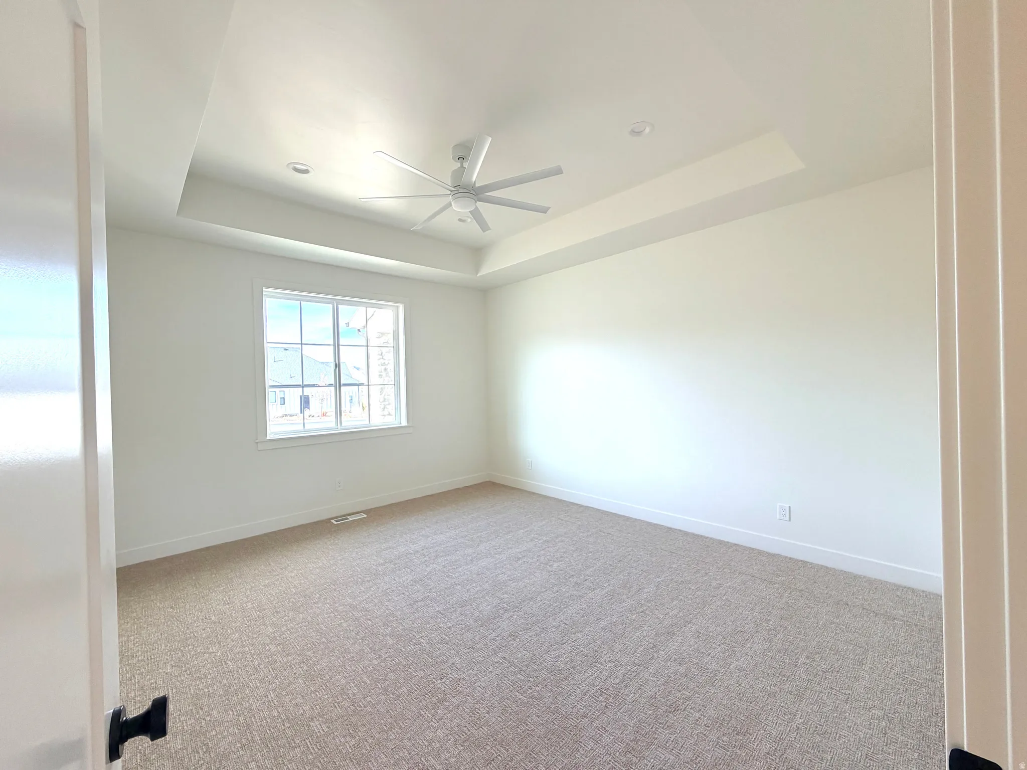 Master bedroom with a tray ceiling, light carpet, and a ceiling fan