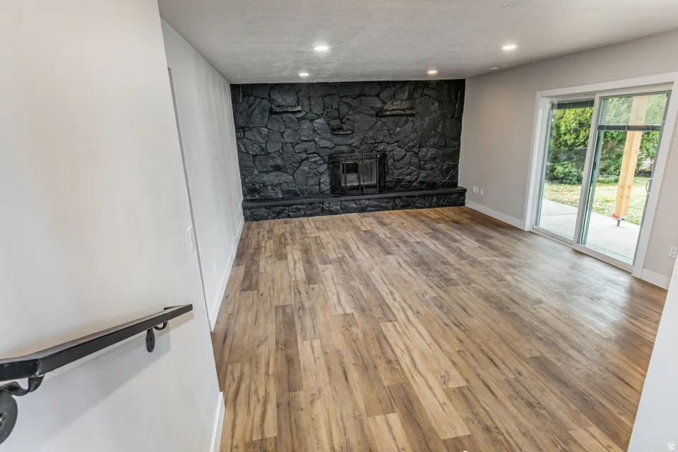 Living room with a textured ceiling, light LVP flooring, a fireplace, and recessed lighting with access to the back yard.