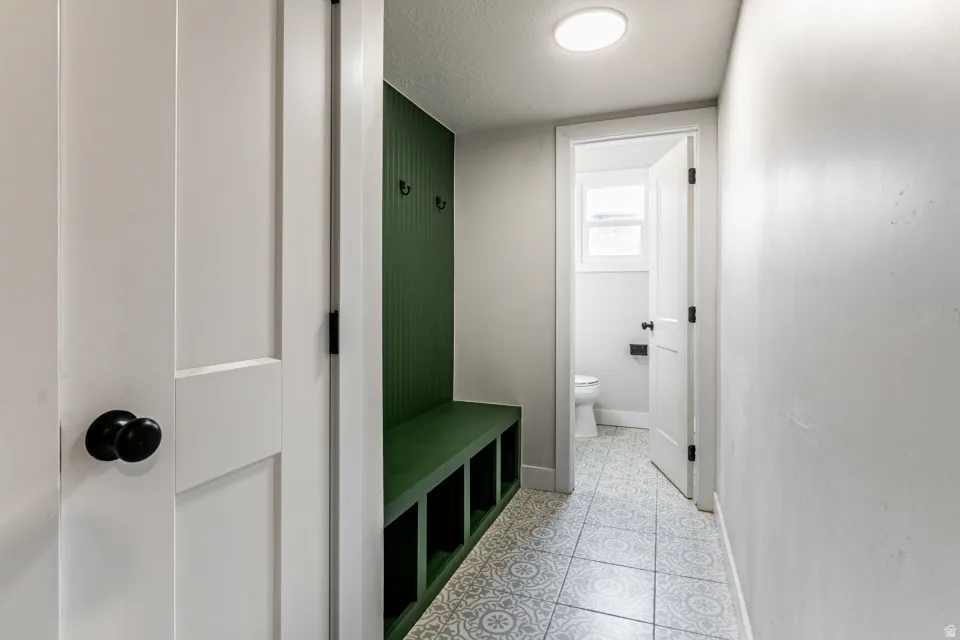 Mudroom from the garage featuring a textured ceiling and light tile patterned flooring with a built in bench.