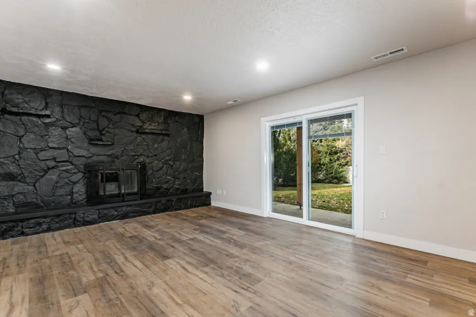 Living room with a textured ceiling, light LVP flooring, a fireplace, and recessed lighting with access to the back yard.