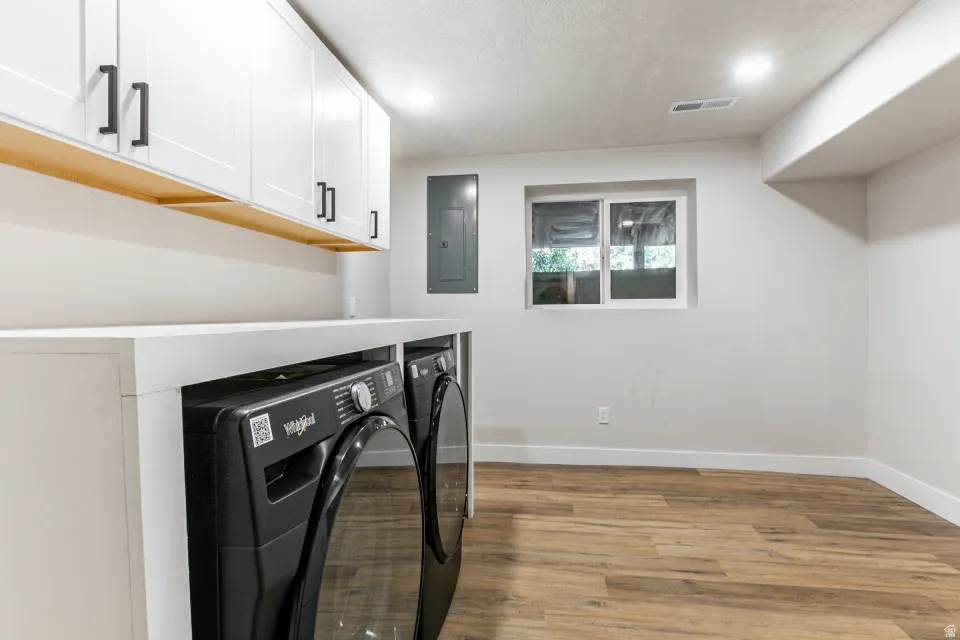 Washroom with light wood finished floors, washer and clothes dryer, electric panel, cabinet space, and recessed lighting and storage space.