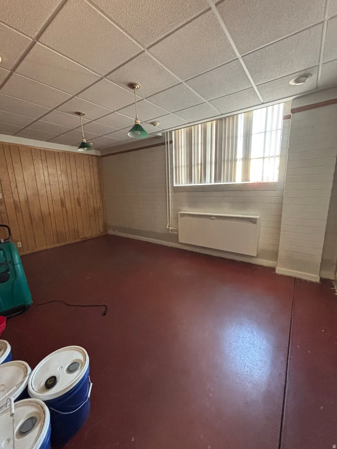 Basement featuring a paneled ceiling, wooden walls, and concrete block wall