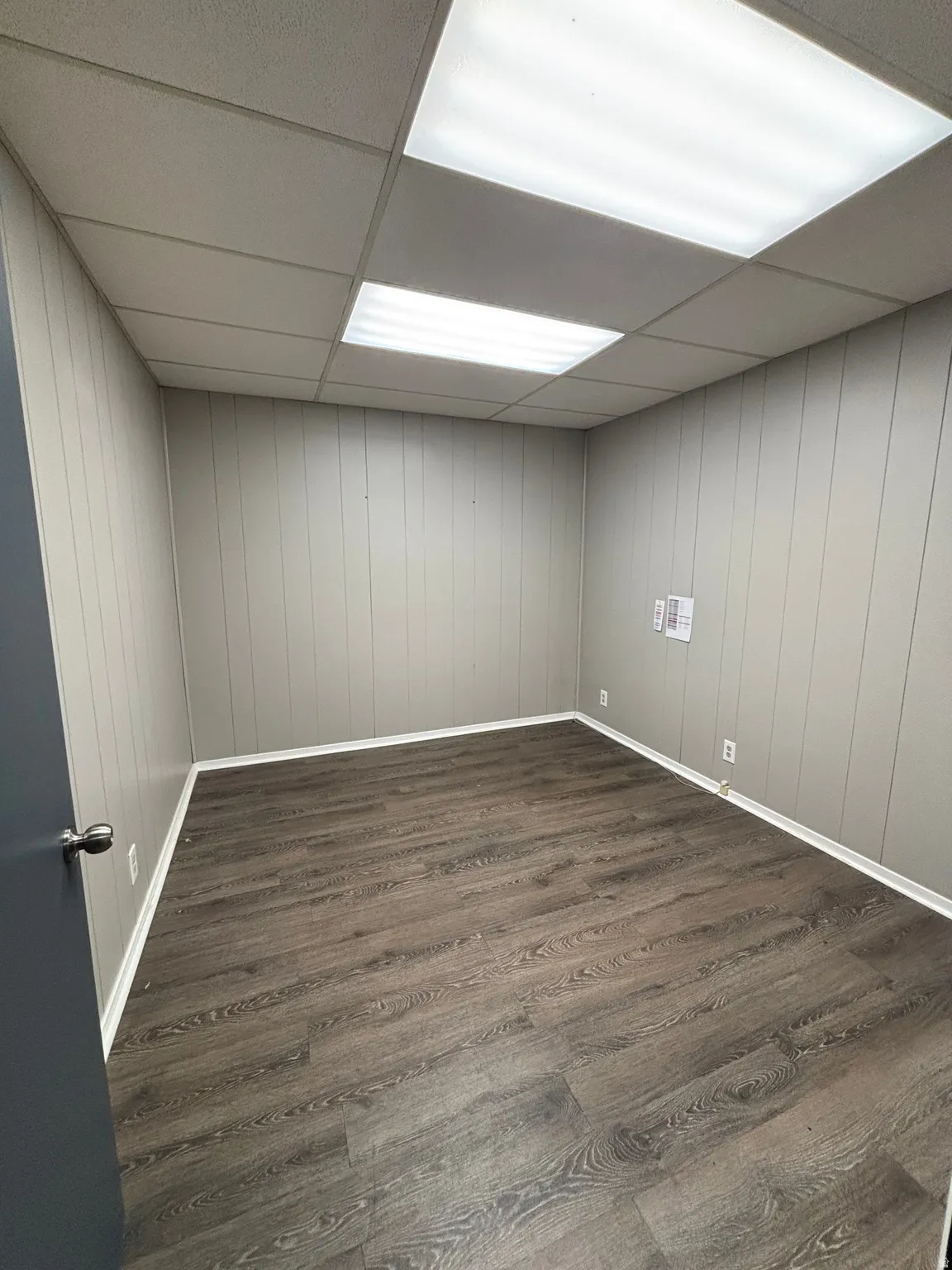 Unfurnished room featuring a drop ceiling, dark wood-style flooring, and wood walls