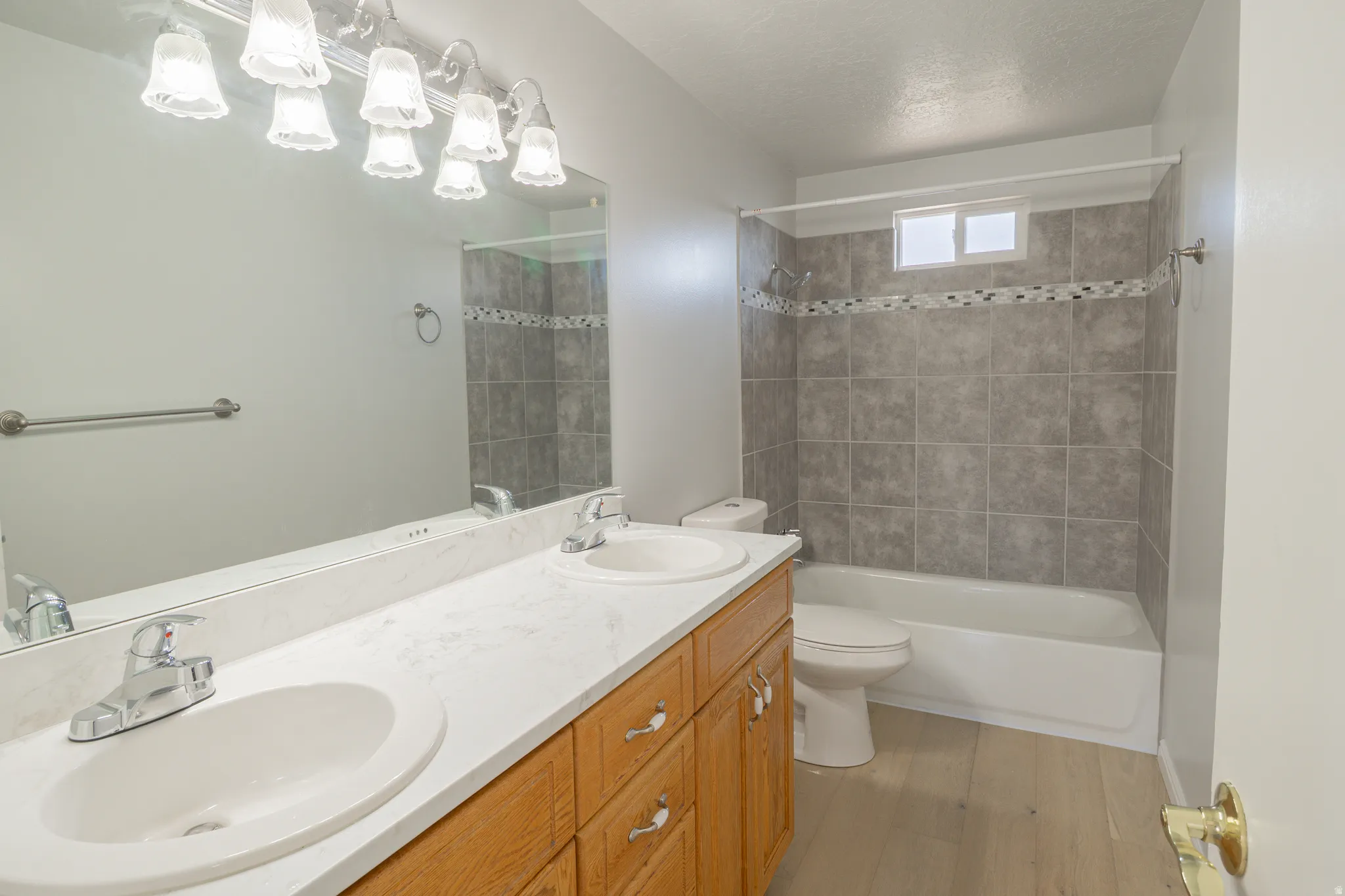 Full bathroom with double vanity, washtub / shower combination, a textured ceiling, and light wood finished floors