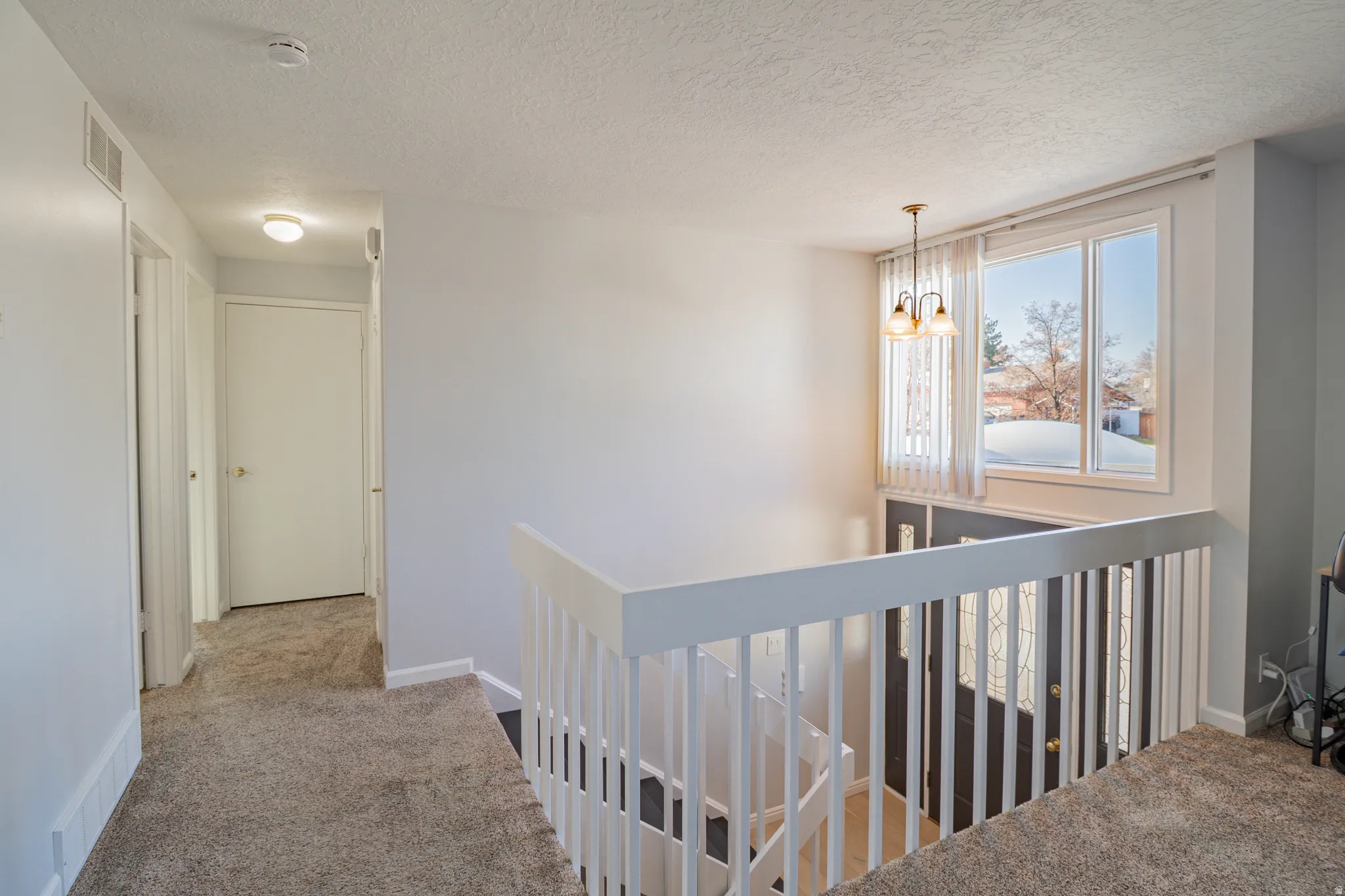 Corridor with a textured ceiling, carpet floors, a chandelier, and an upstairs landing
