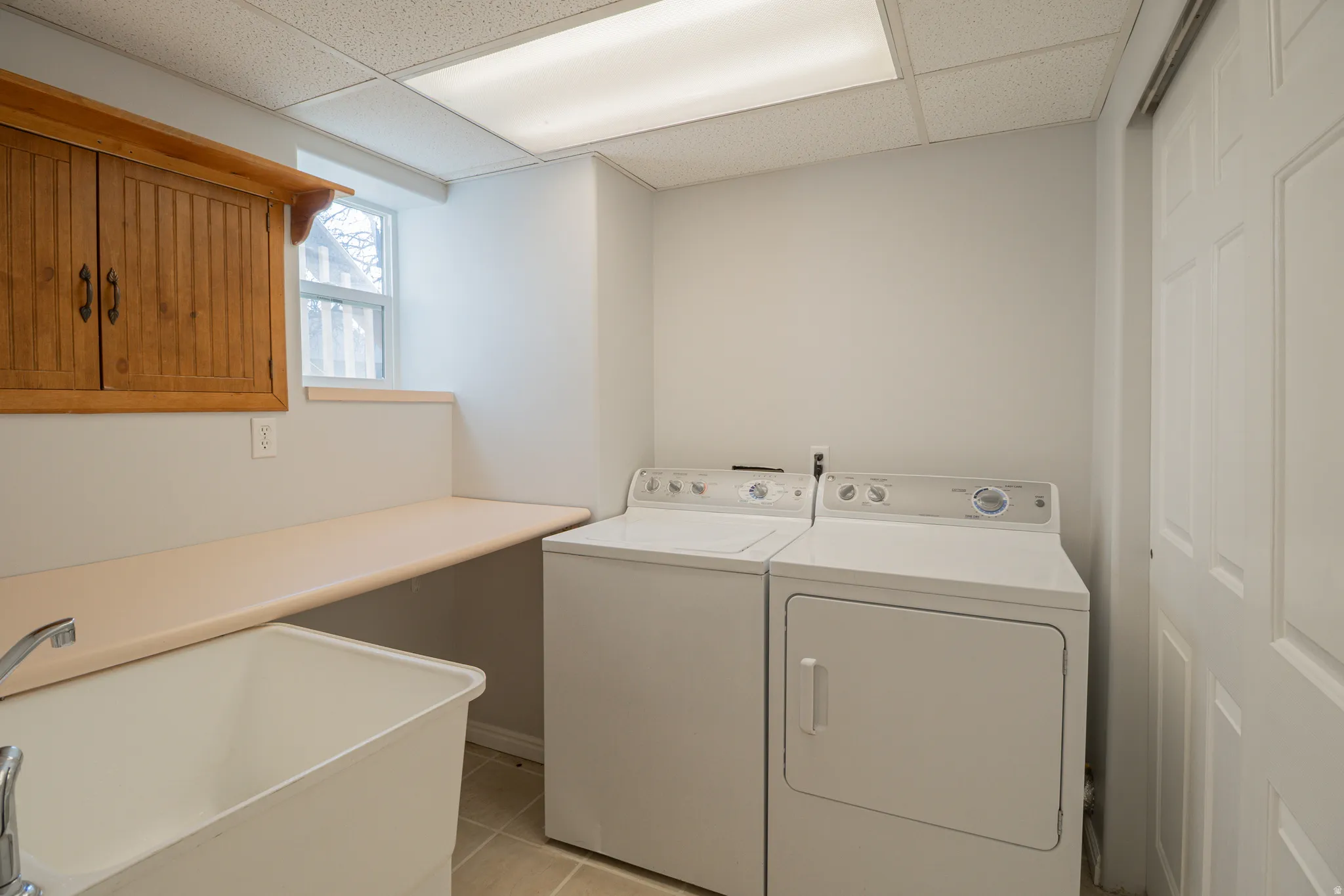 Laundry area featuring a paneled ceiling, light tile patterned floors, separate washer and dryer, and cabinet space