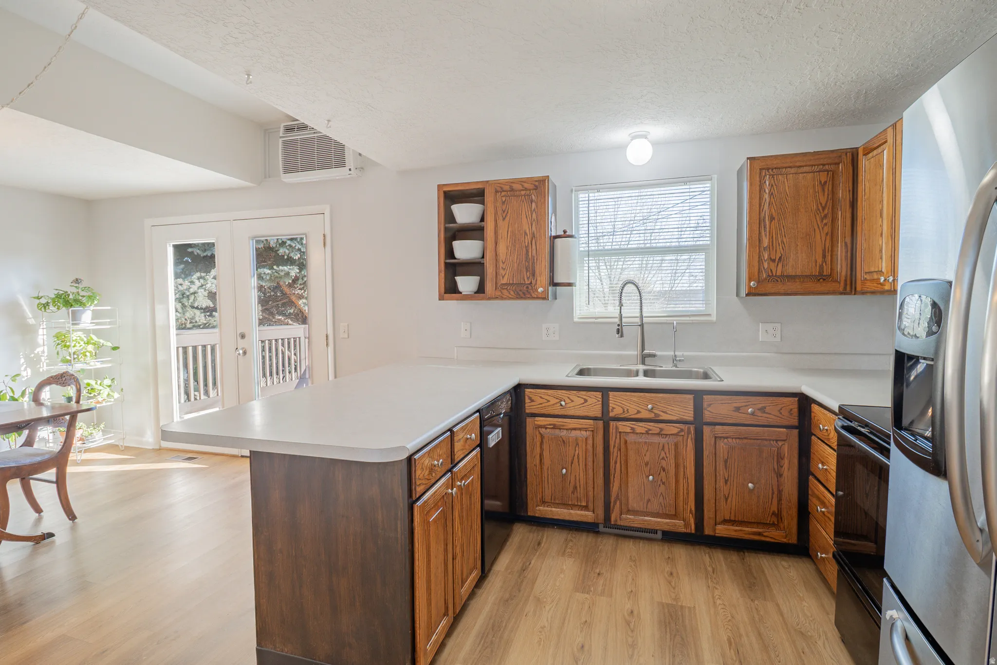 Kitchen featuring brown cabinetry, black appliances, french doors, a peninsula, and a textured ceiling