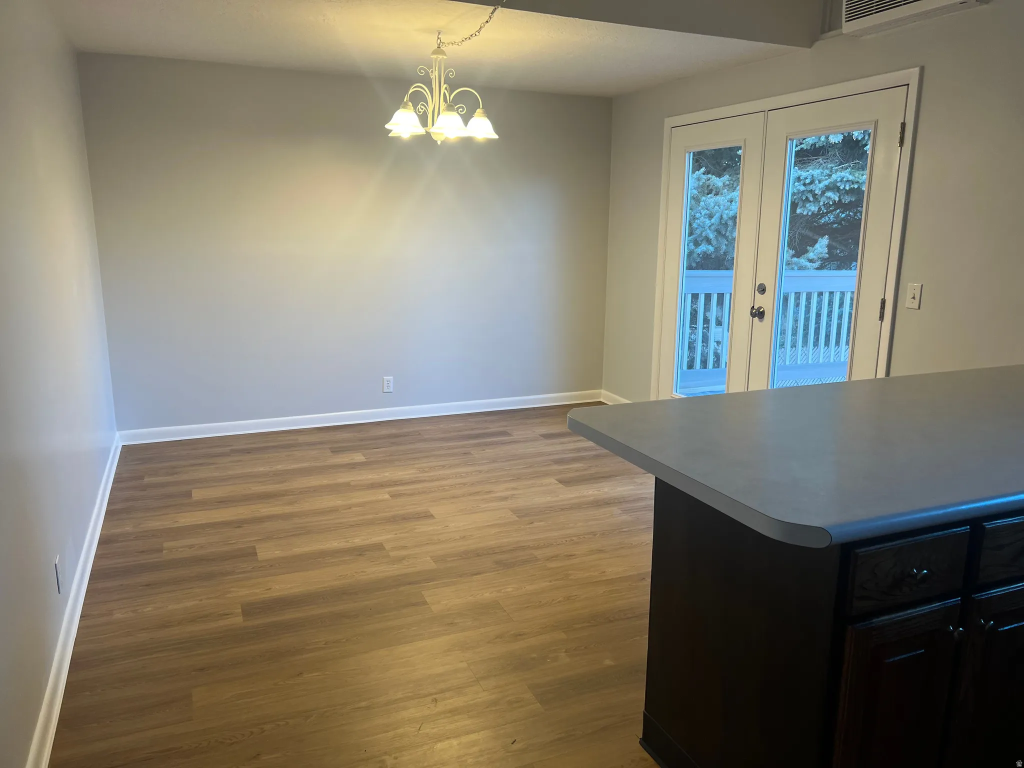 Unfurnished dining area with dark wood-style floors, a chandelier, and french doors