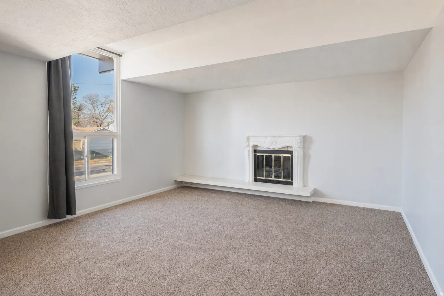 Living area featuring plush carpeting, light gray wall tones, a decorative fireplace with an ornate mantel, and a large window providing natural light