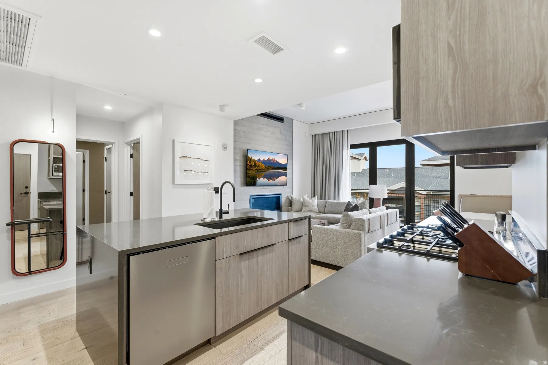 Kitchen with modern cabinets, dark stone counters, light wood finished floors, a kitchen island with sink, and stainless steel dishwasher