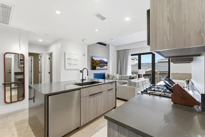 Kitchen with modern cabinets, dark stone counters, light wood finished floors, a kitchen island with sink, and stainless steel dishwasher