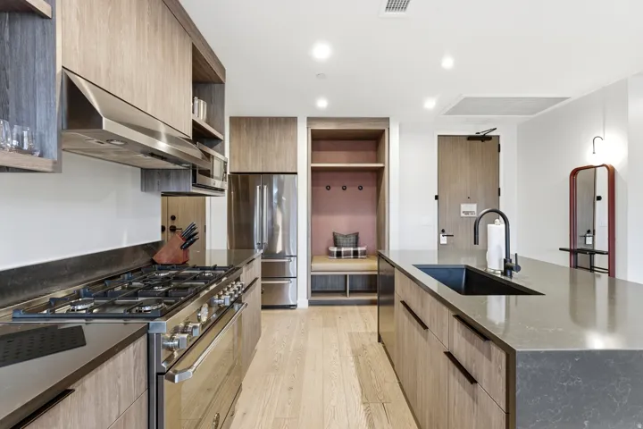 Kitchen with appliances with stainless steel finishes, modern cabinets, under cabinet range hood, light brown cabinets, and dark stone counters
