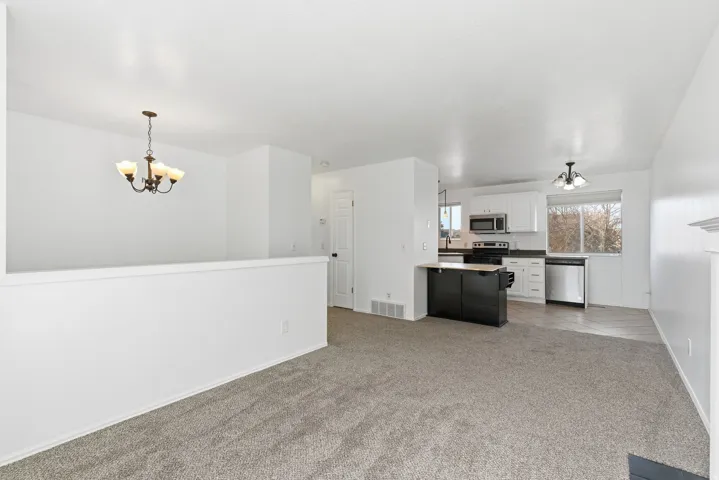 Kitchen featuring a chandelier, light colored carpet, white cabinetry, pendant lighting, and stainless steel appliances