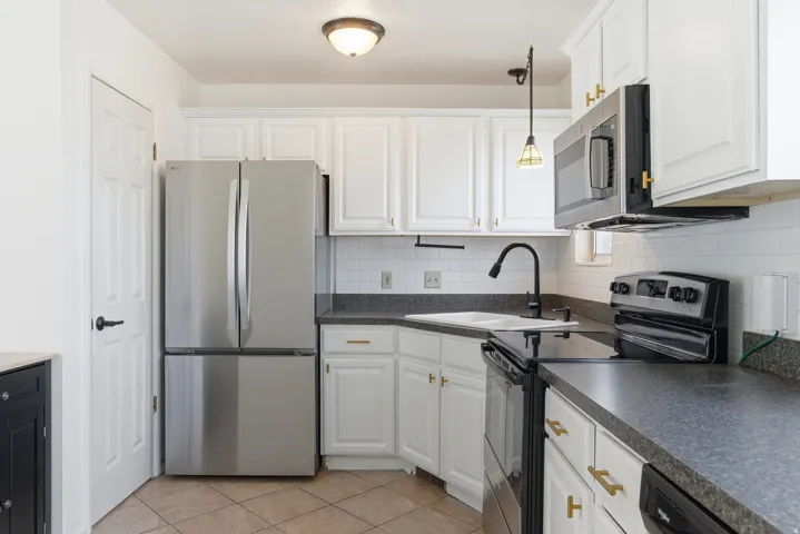 Kitchen with appliances with stainless steel finishes, decorative light fixtures, decorative backsplash, white cabinetry, and light tile patterned flooring