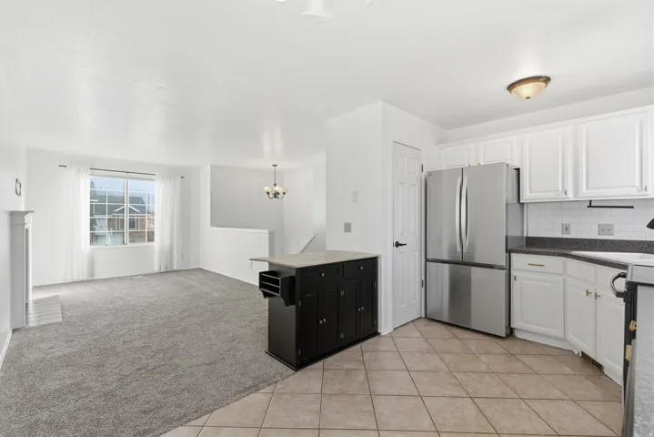 Kitchen with appliances with stainless steel finishes, white cabinetry, open floor plan, a chandelier, and light carpet