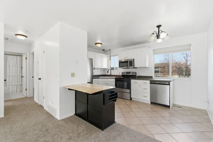 Kitchen featuring butcher block countertops, appliances with stainless steel finishes, white cabinets, light colored carpet, and light tile patterned floors