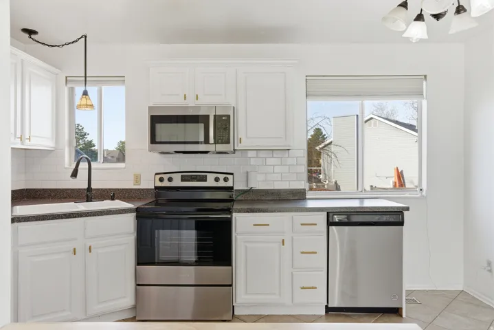 Kitchen with hanging light fixtures, appliances with stainless steel finishes, dark countertops, white cabinets, and decorative backsplash