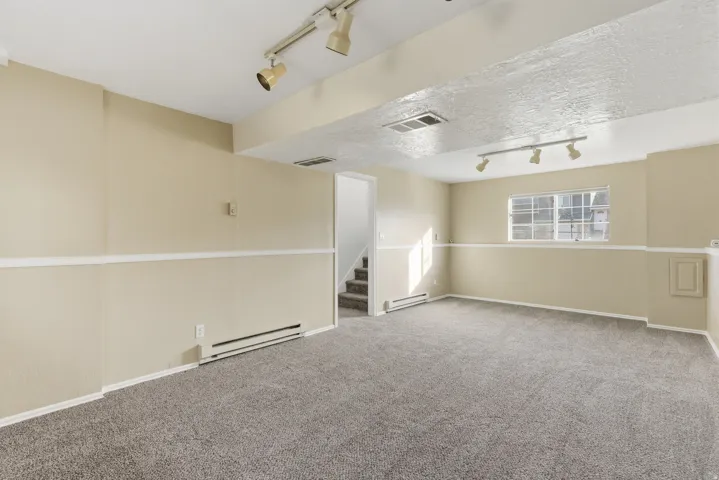 Empty room with rail lighting, a baseboard heating unit, carpet floors, a textured ceiling, and stairs