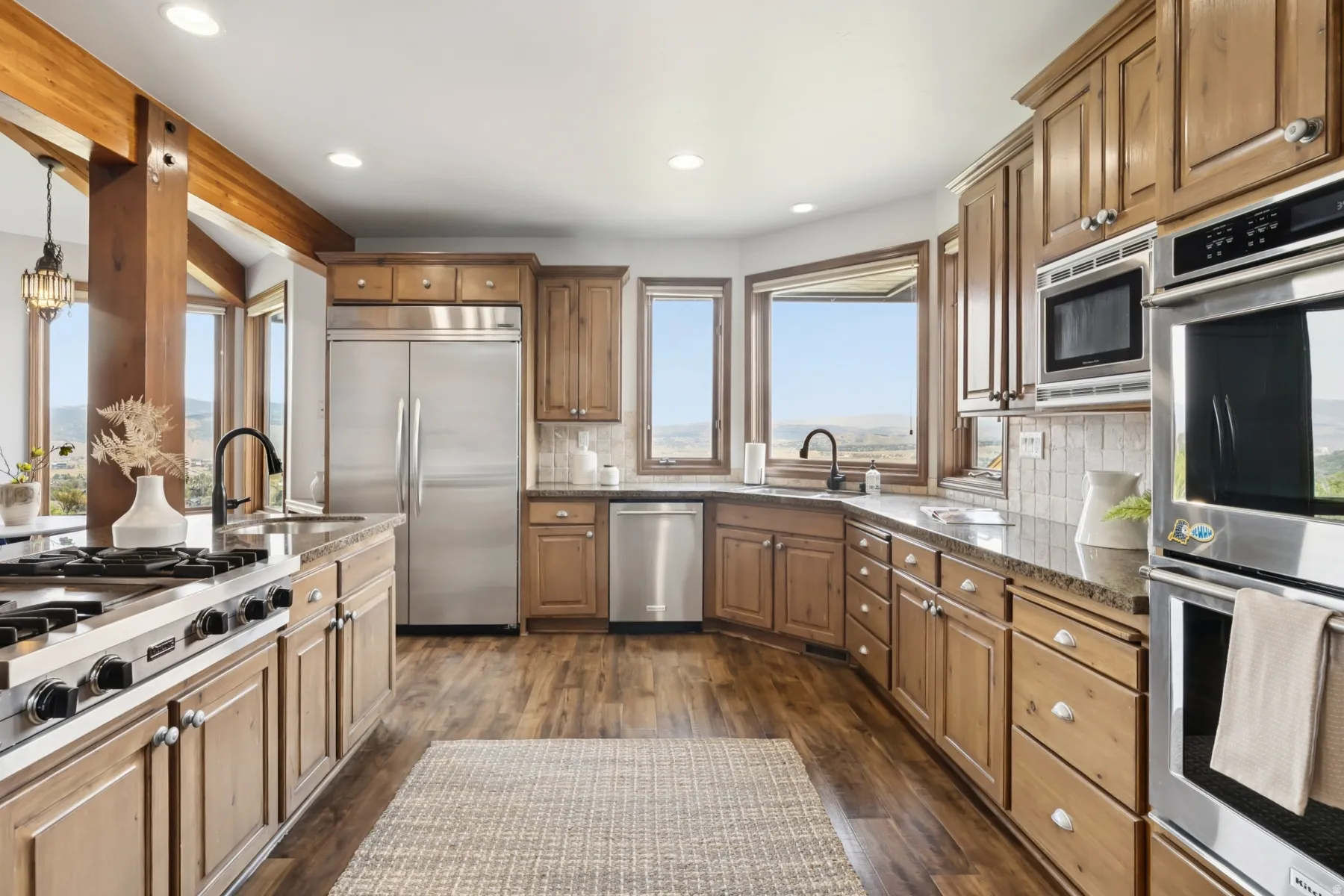 Kitchen featuring built in appliances, dark wood-style floors, dark stone countertops, recessed lighting, and decorative light fixtures