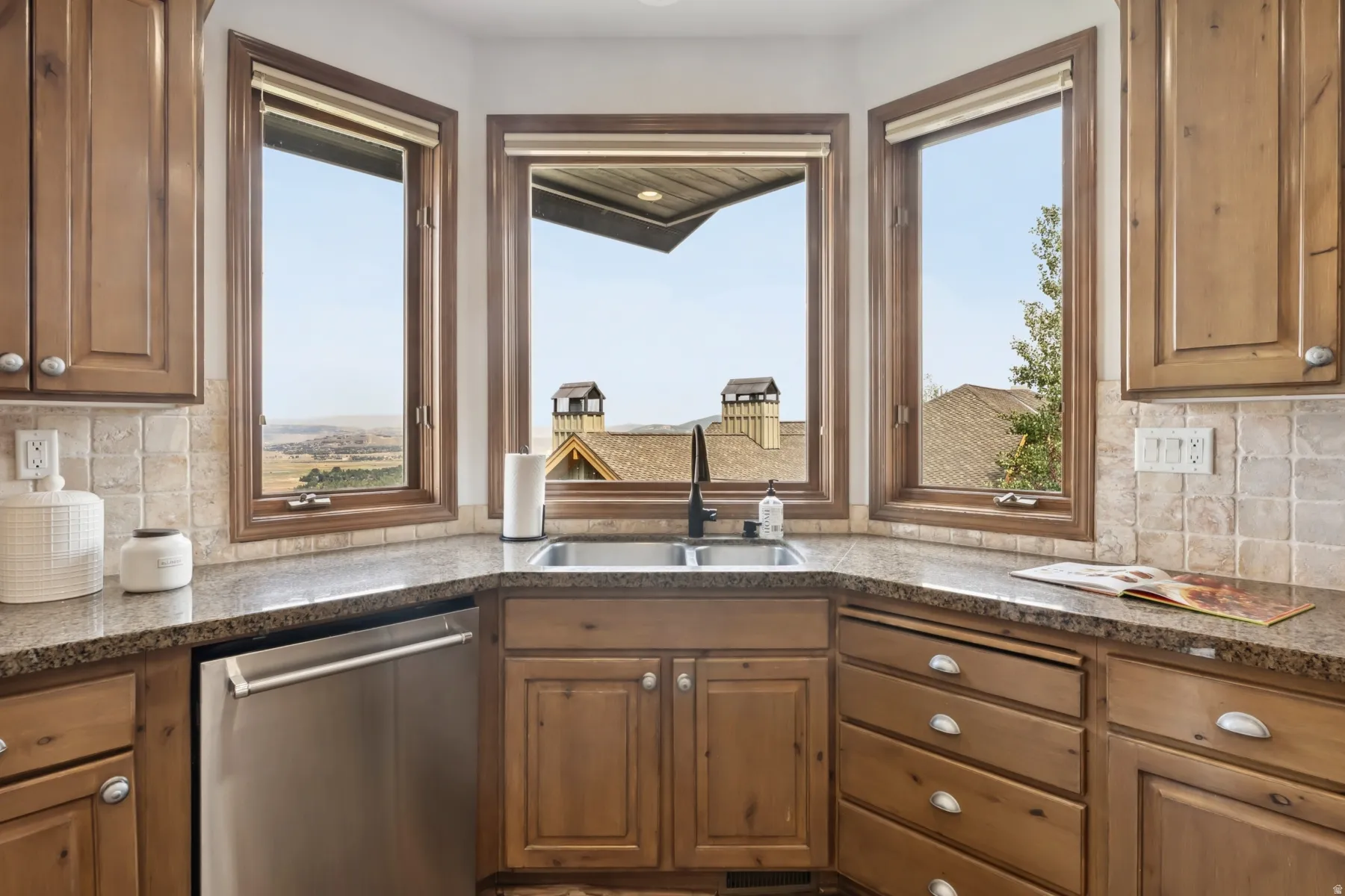 Kitchen featuring backsplash, stainless steel dishwasher, brown cabinets, and dark stone counters