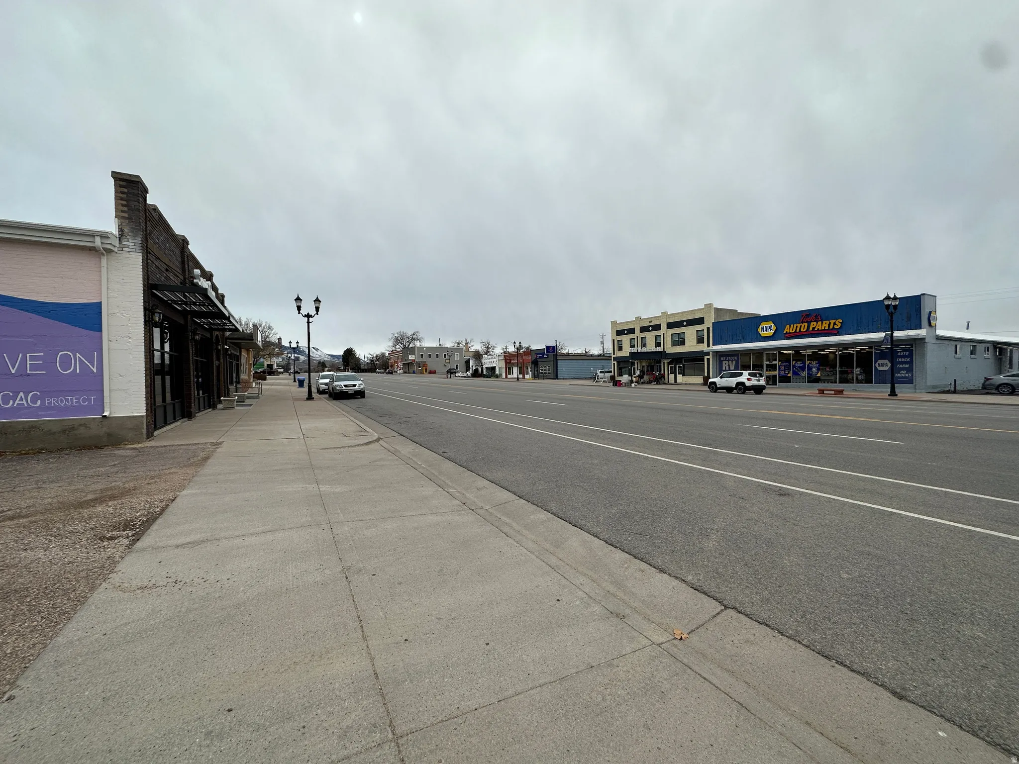 View of asphalt road featuring sidewalks, curbs, and street lighting