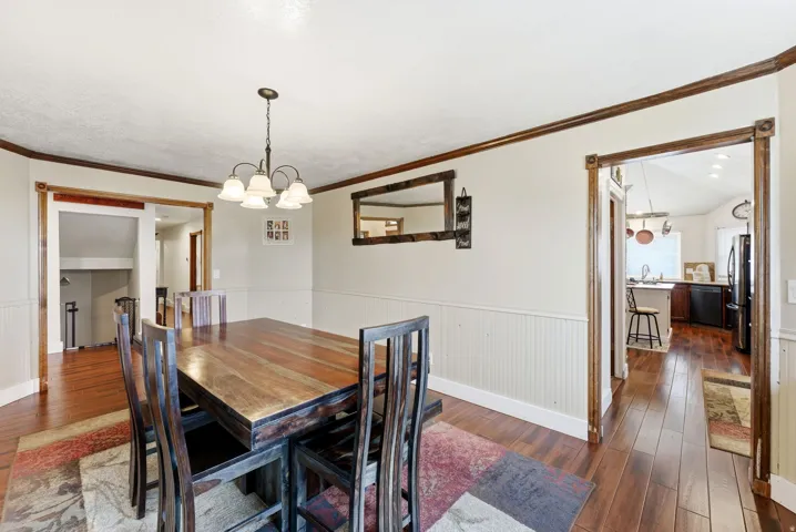 Dining area with dark wood-style floors, a wainscoted wall, a chandelier, and crown molding
