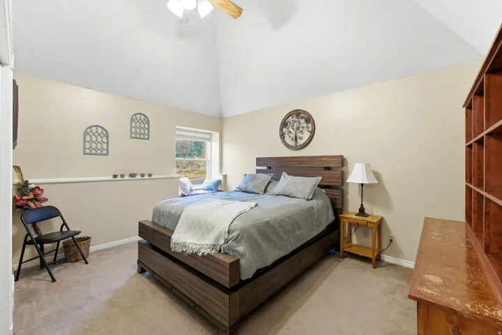 Bedroom featuring light colored carpet, lofted ceiling, and a ceiling fan