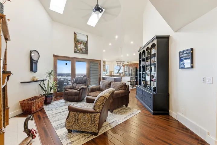 Living area featuring dark wood-style flooring, a skylight, high vaulted ceiling, and a ceiling fan