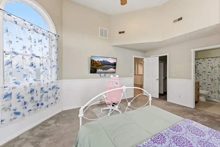 Bedroom with a spacious closet, carpet floors, a ceiling fan, ensuite bathroom, and a towering ceiling