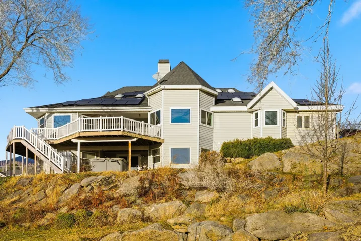 Back of property with a wooden deck, stairs, solar panels, a chimney, and a shingled roof
