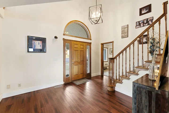 Foyer entrance featuring dark wood-style flooring, a chandelier, stairway, and a high ceiling