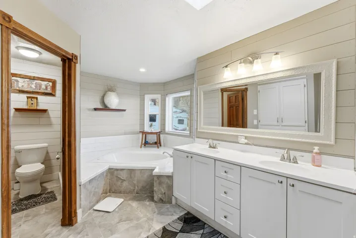 Full bathroom with double vanity, a bath, wooden walls, and recessed lighting