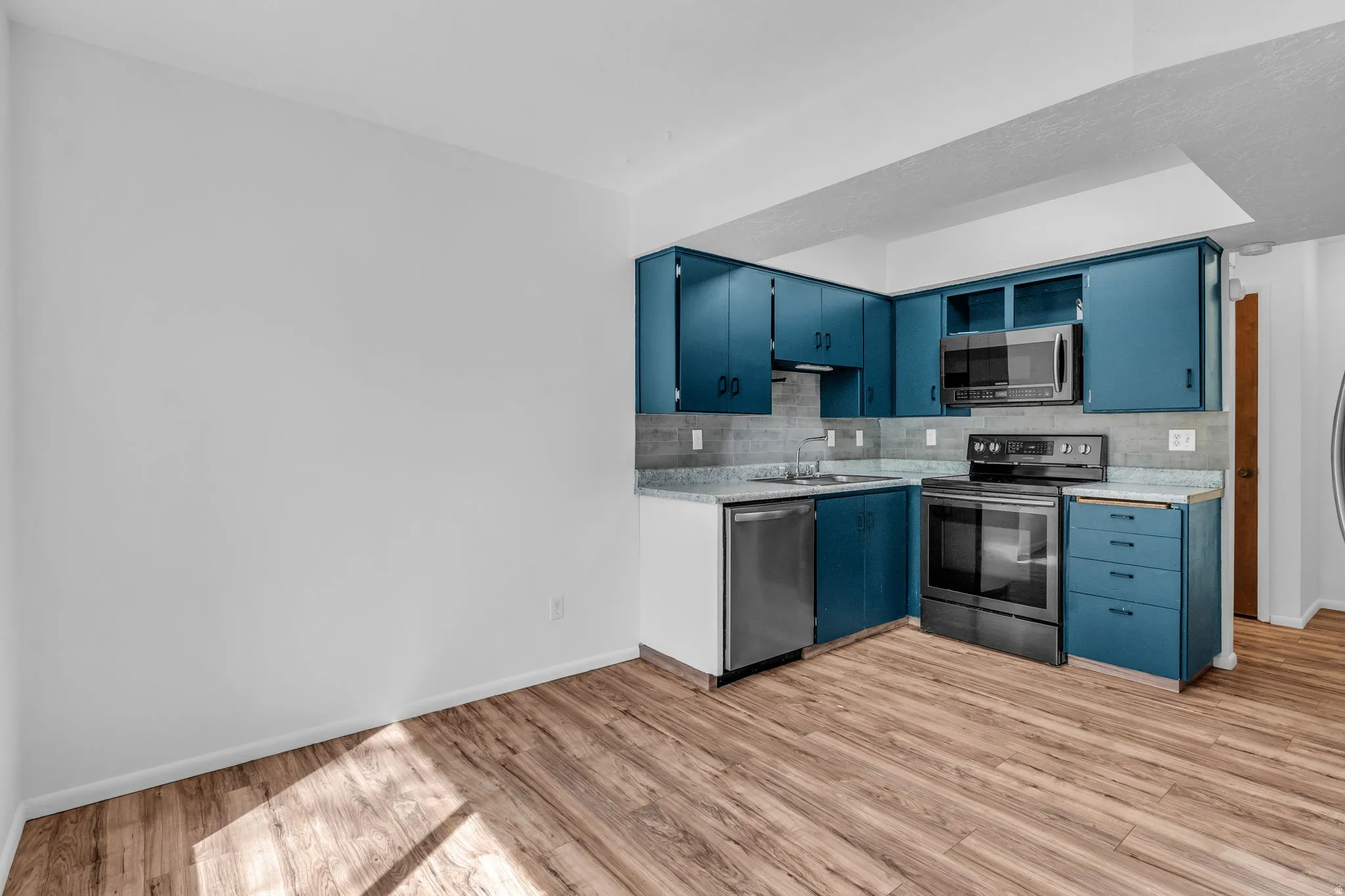 Kitchen featuring blue cabinetry, stainless steel appliances, light wood-style floors, decorative backsplash, and light stone countertops