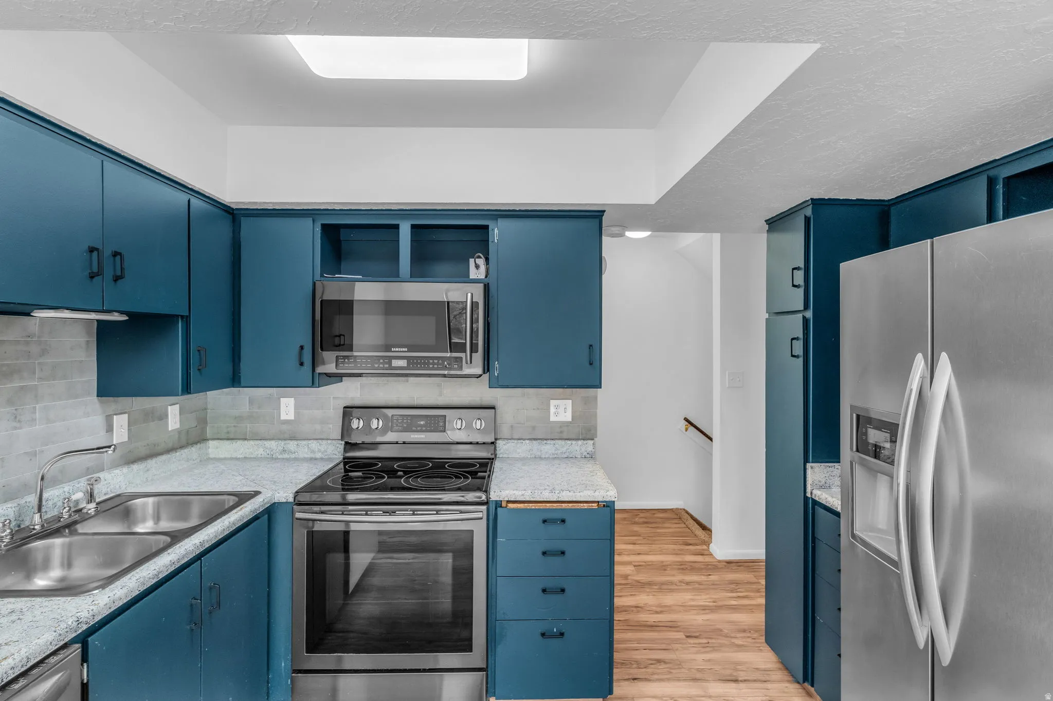 Kitchen featuring blue cabinets, stainless steel appliances, open shelves, light wood finished floors, and backsplash