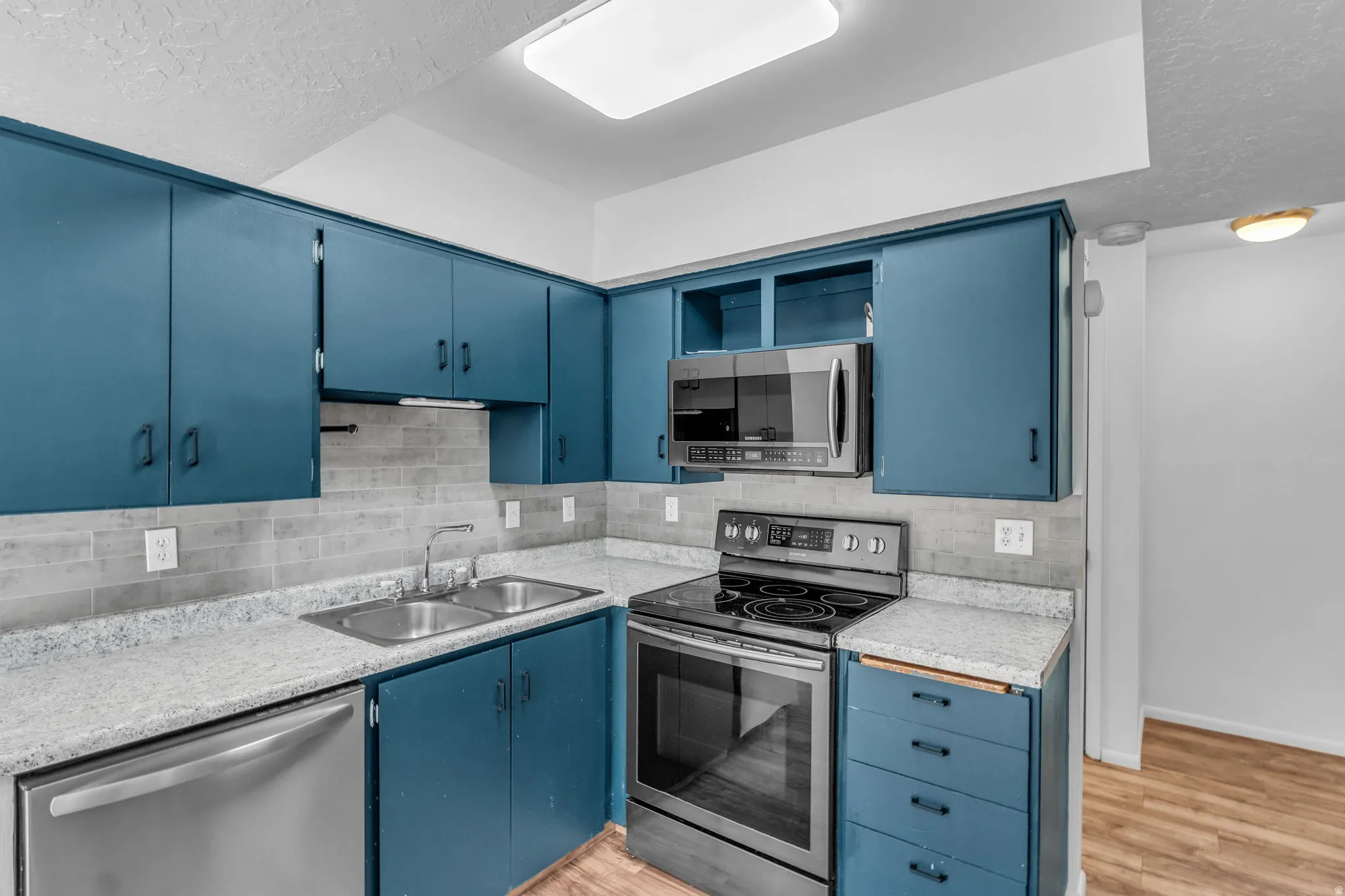 Kitchen with blue cabinets, stainless steel appliances, light countertops, a textured ceiling, and backsplash
