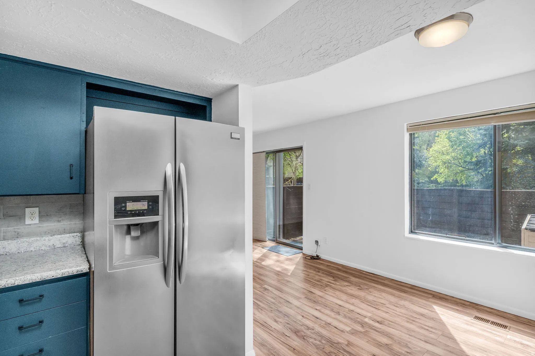 Kitchen featuring stainless steel fridge with ice dispenser, light wood finished floors, blue cabinetry, and a textured ceiling