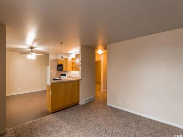 Kitchen featuring open floor plan, dark colored carpet, a ceiling fan, hanging light fixtures, and light countertops