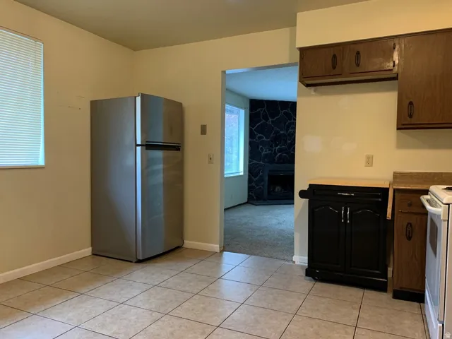 Kitchen with freestanding refrigerator, white stove, light countertops, a stone fireplace, and light tile patterned floors