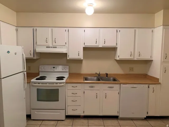 Kitchen featuring white appliances, white cabinets, light countertops, and under cabinet range hood