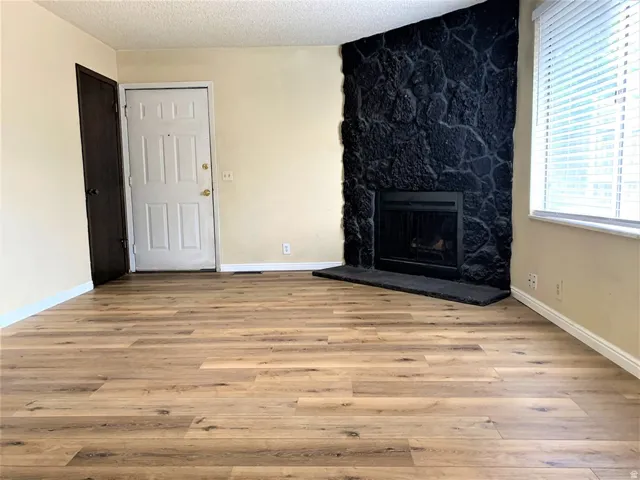 Unfurnished living room featuring a stone fireplace, light wood-style floors, and a textured ceiling