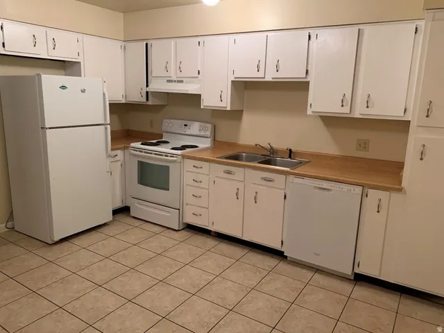 Kitchen with white appliances, light countertops, white cabinets, and under cabinet range hood