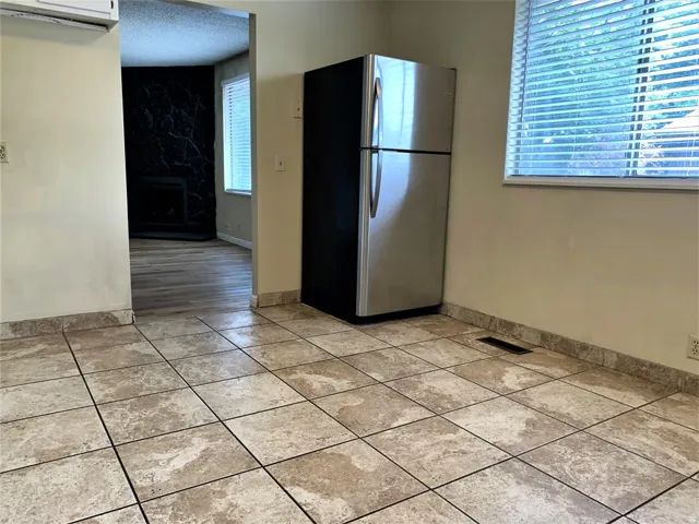 Kitchen with freestanding refrigerator, a fireplace, an AC wall unit, a textured ceiling, and light tile patterned floors