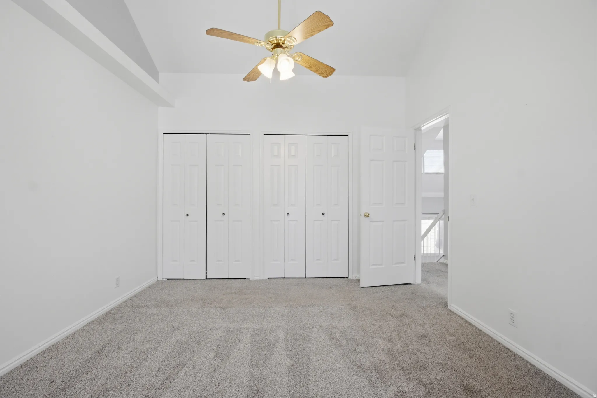 Unfurnished bedroom featuring multiple closets, vaulted ceiling, carpet floors, and ceiling fan