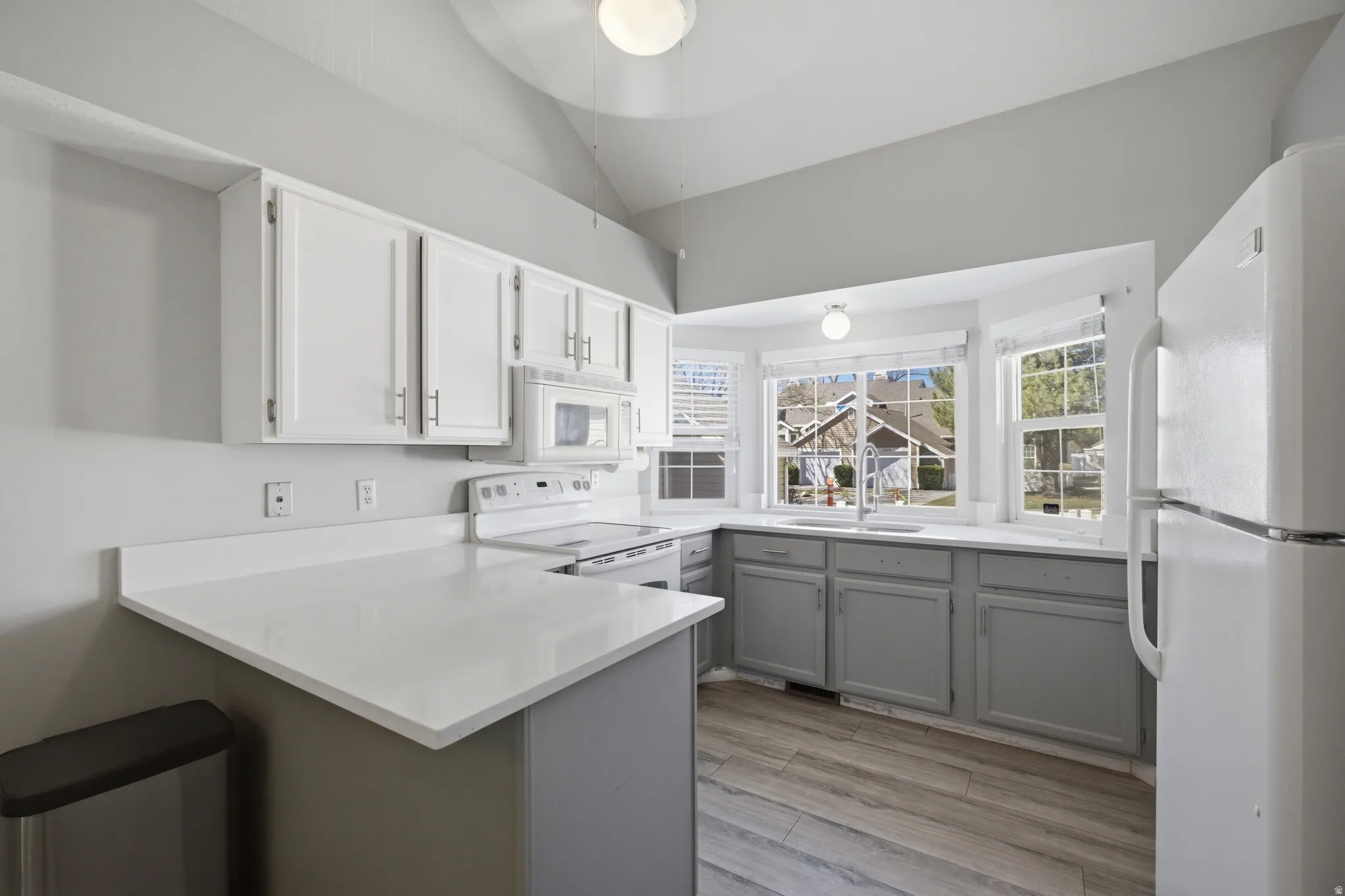 Kitchen with white appliances, a peninsula, light wood-style flooring, lofted ceiling, and a ceiling fan