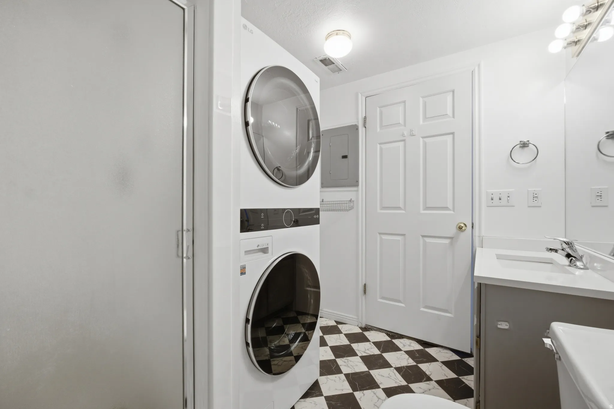 Laundry area with dark flooring, stacked washer and clothes dryer, and electric panel