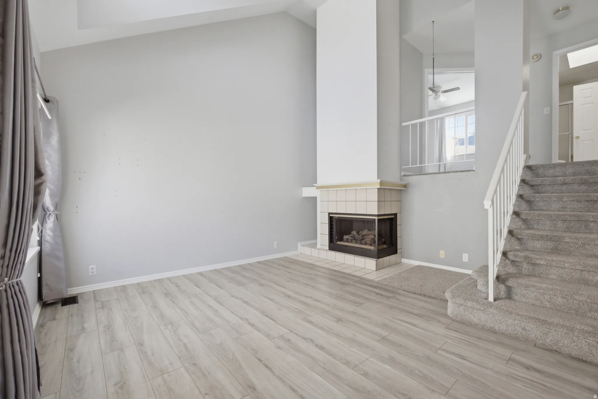 Unfurnished living room with a ceiling fan, lofted ceiling, light wood finished floors, and a tiled fireplace