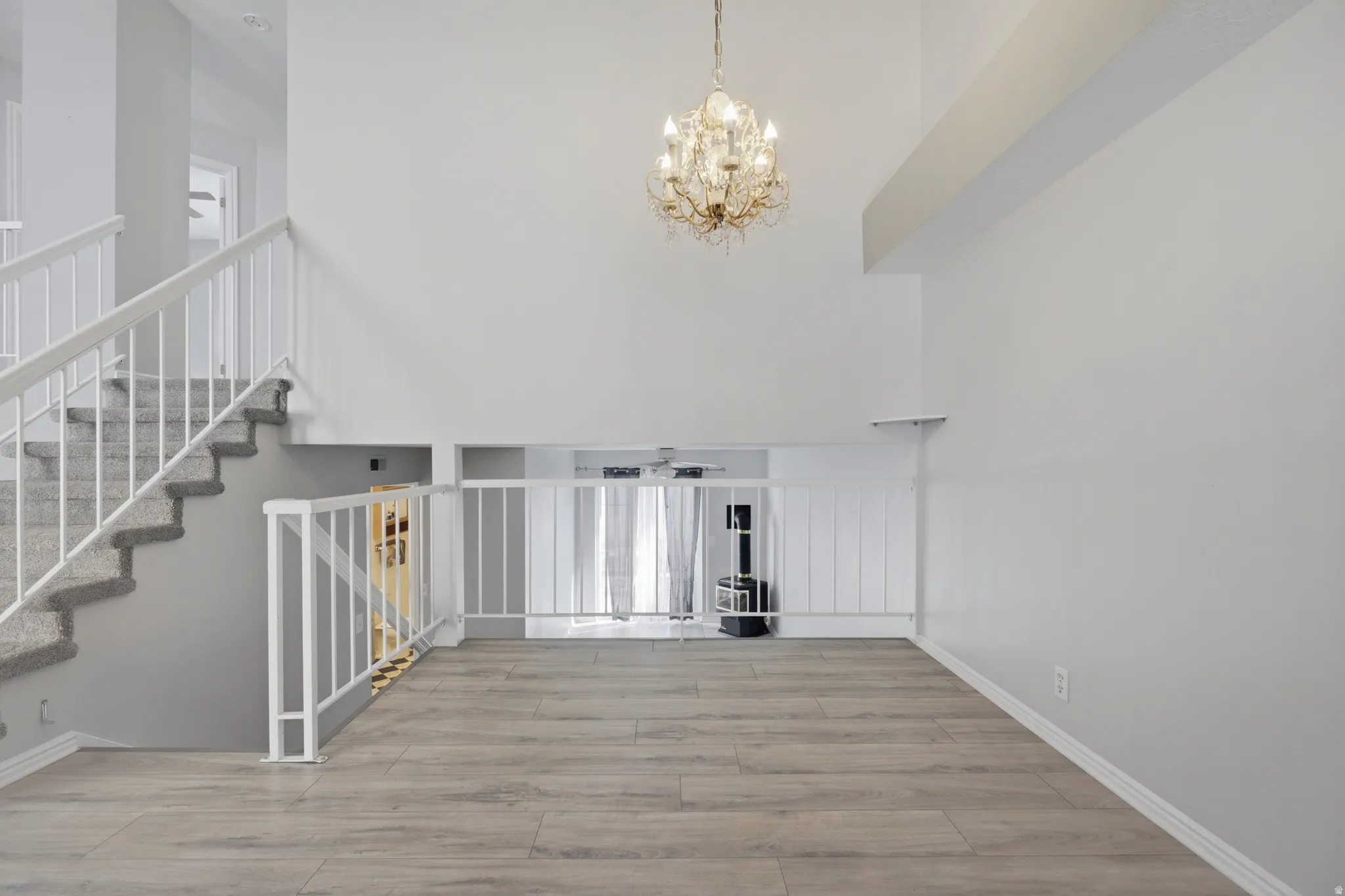 Unfurnished living room featuring suspended lighting, light wood-type flooring, and a high ceiling